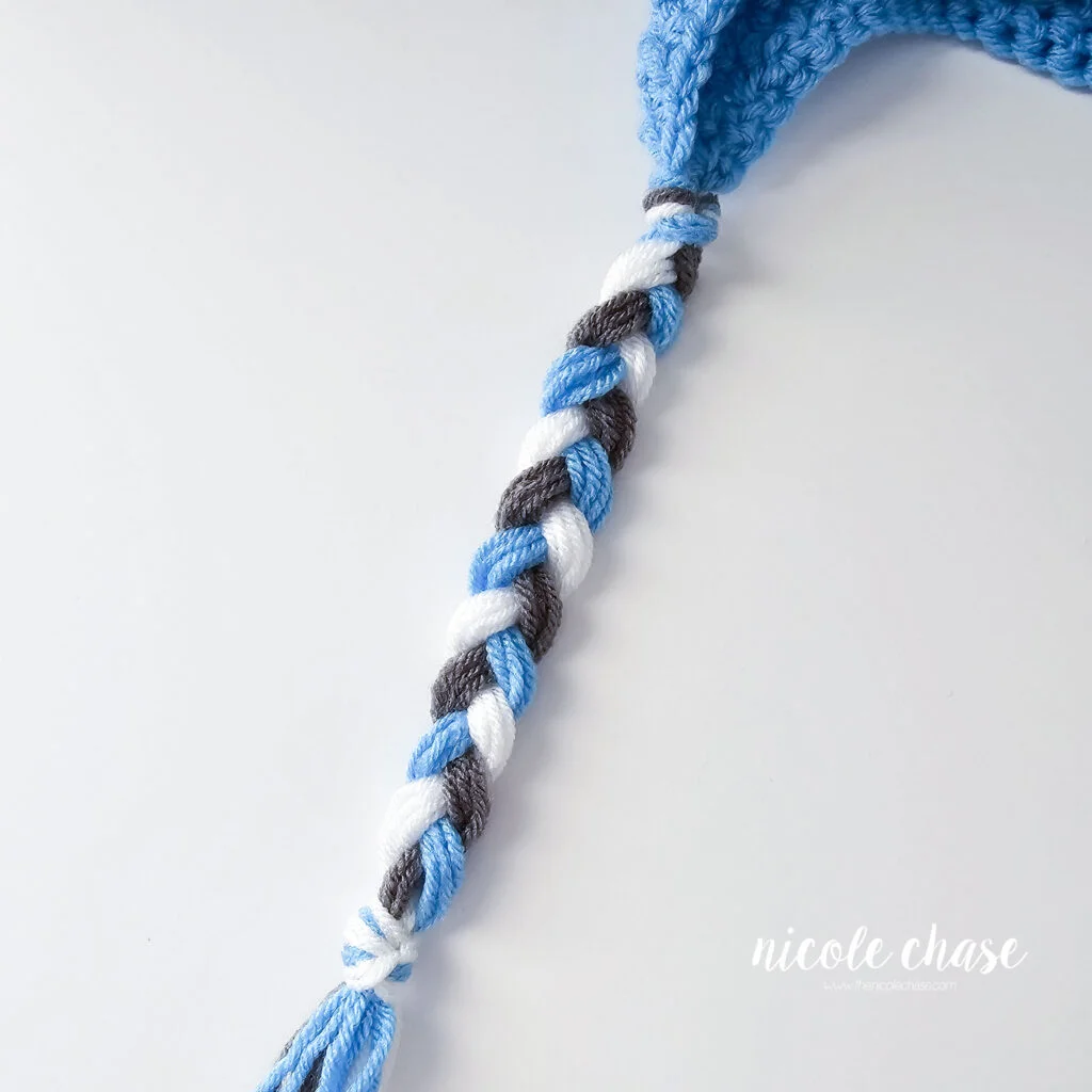 Braiding the tassels for the crochet hat with earflaps, step 2.