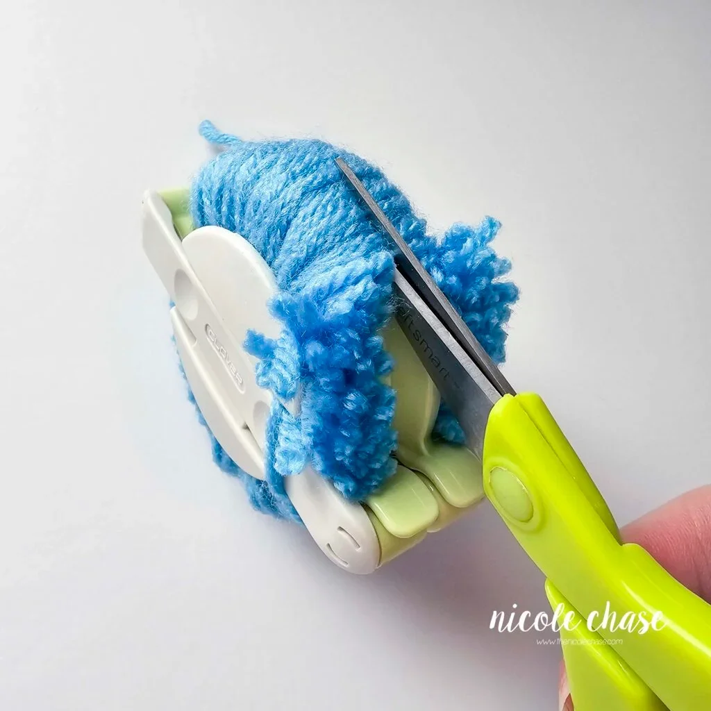Cutting the blue yarn in the pom maker. 