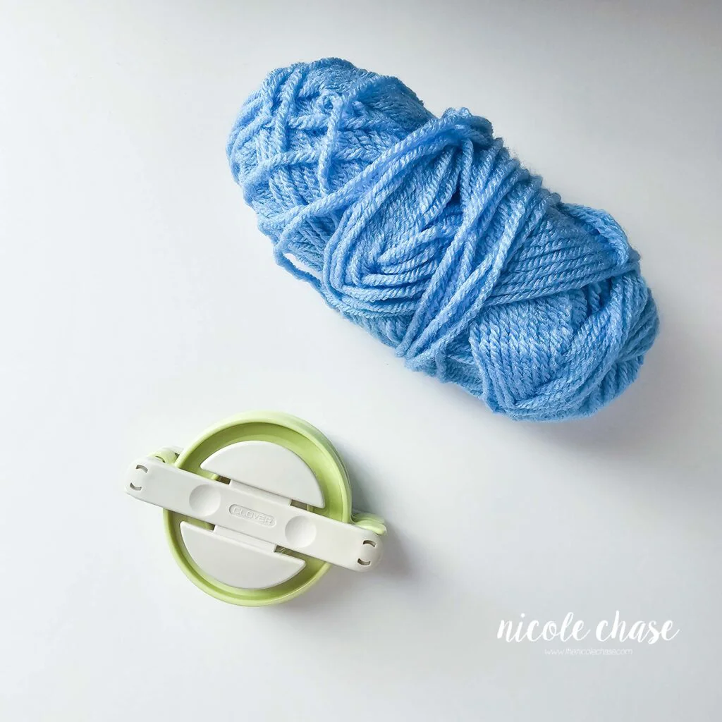 Skein of blue yarn next to a pom maker. 