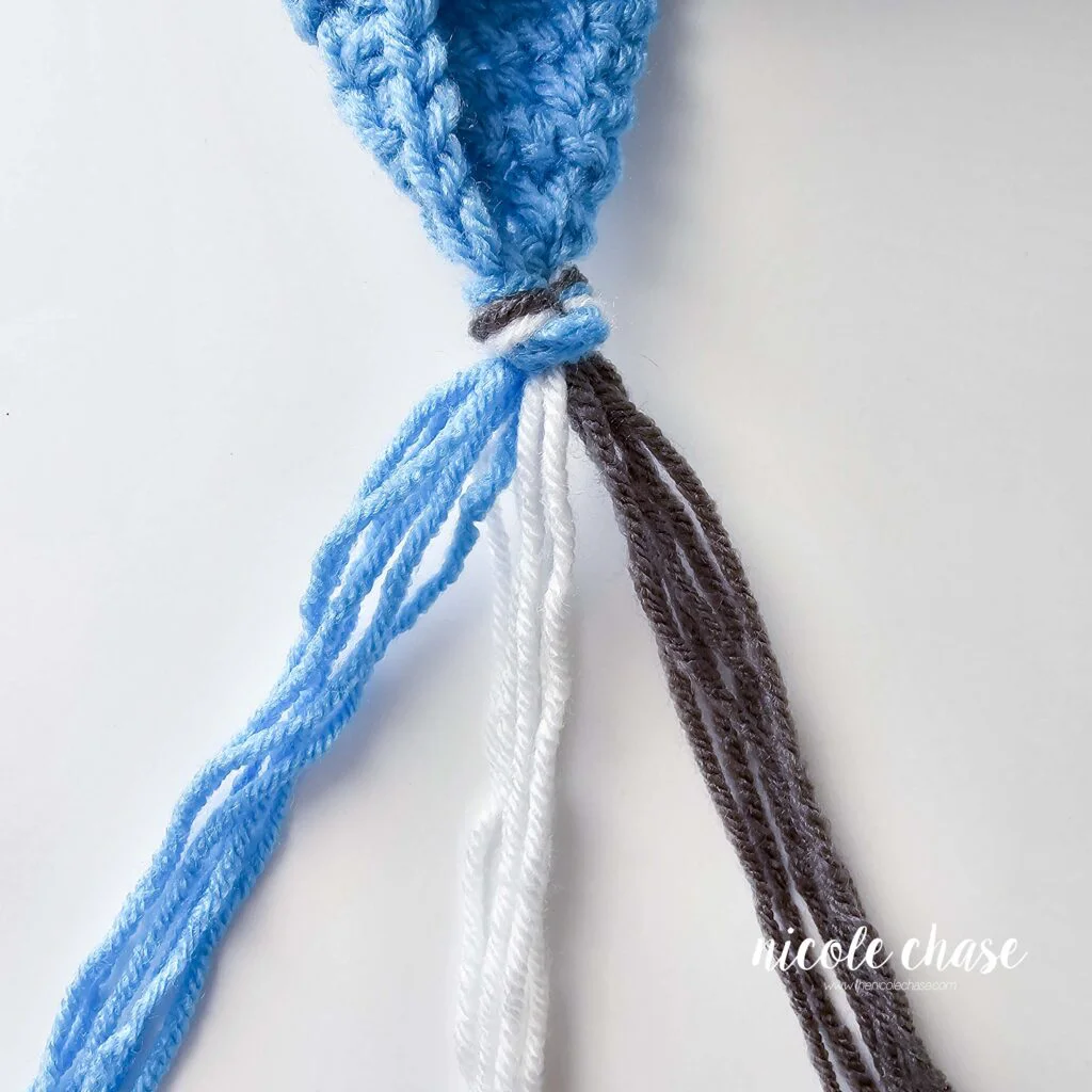 Braiding the tassels for the crochet hat with earflaps, step 1. 