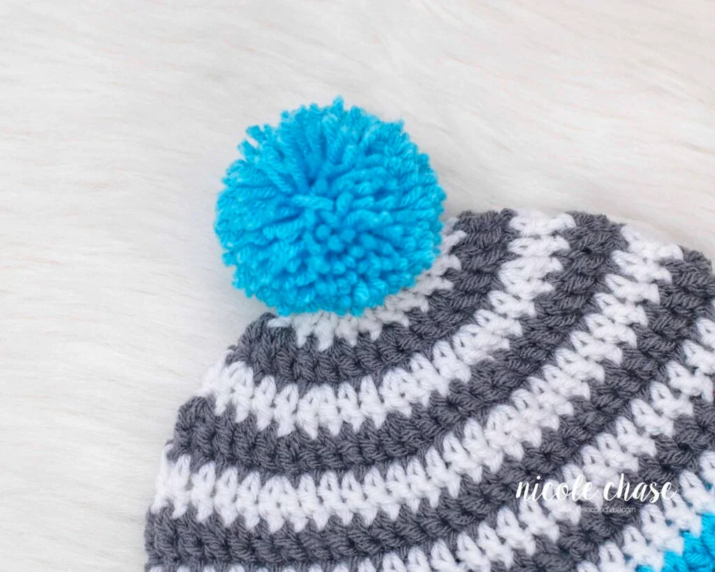 Close up of the blue pom pom attached to the top of the free earflap hat crochet pattern. 