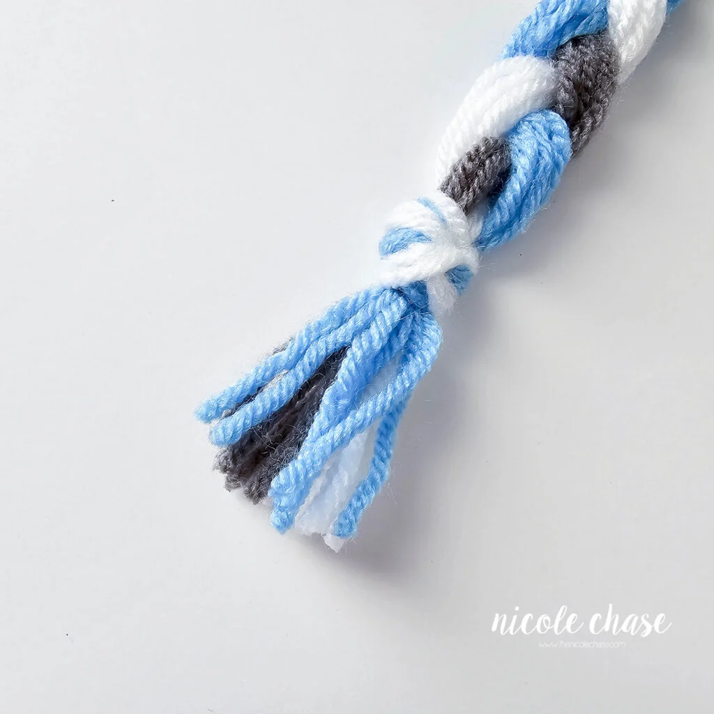 Braiding the tassels for the crochet hat with earflaps, step 3.