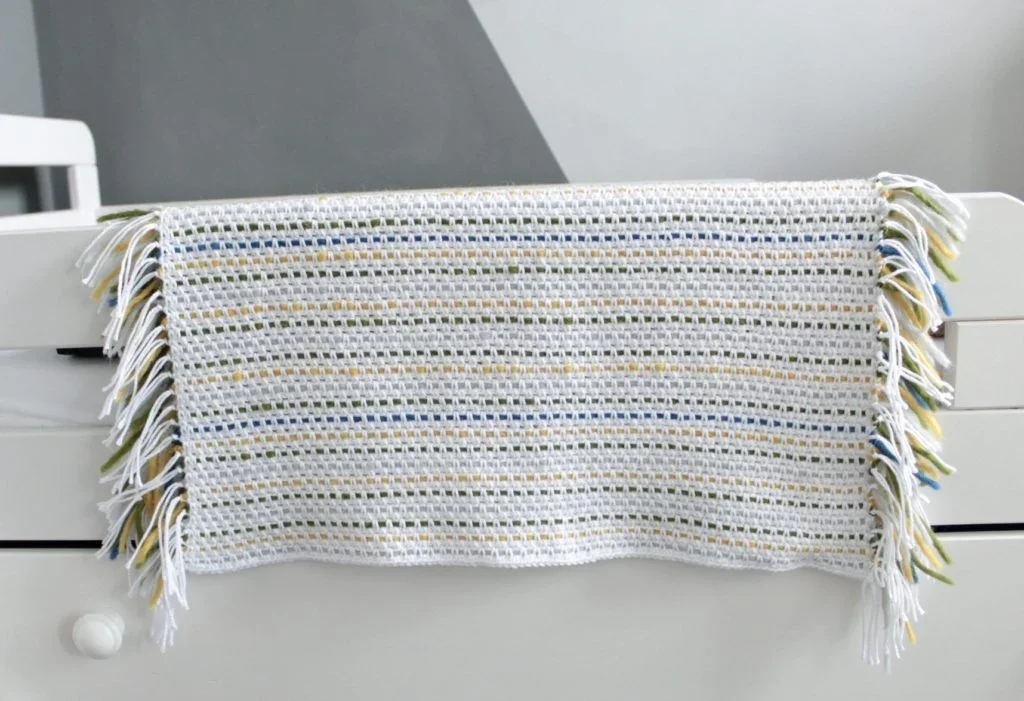 woven crochet baby blanket draped over side bar of bed