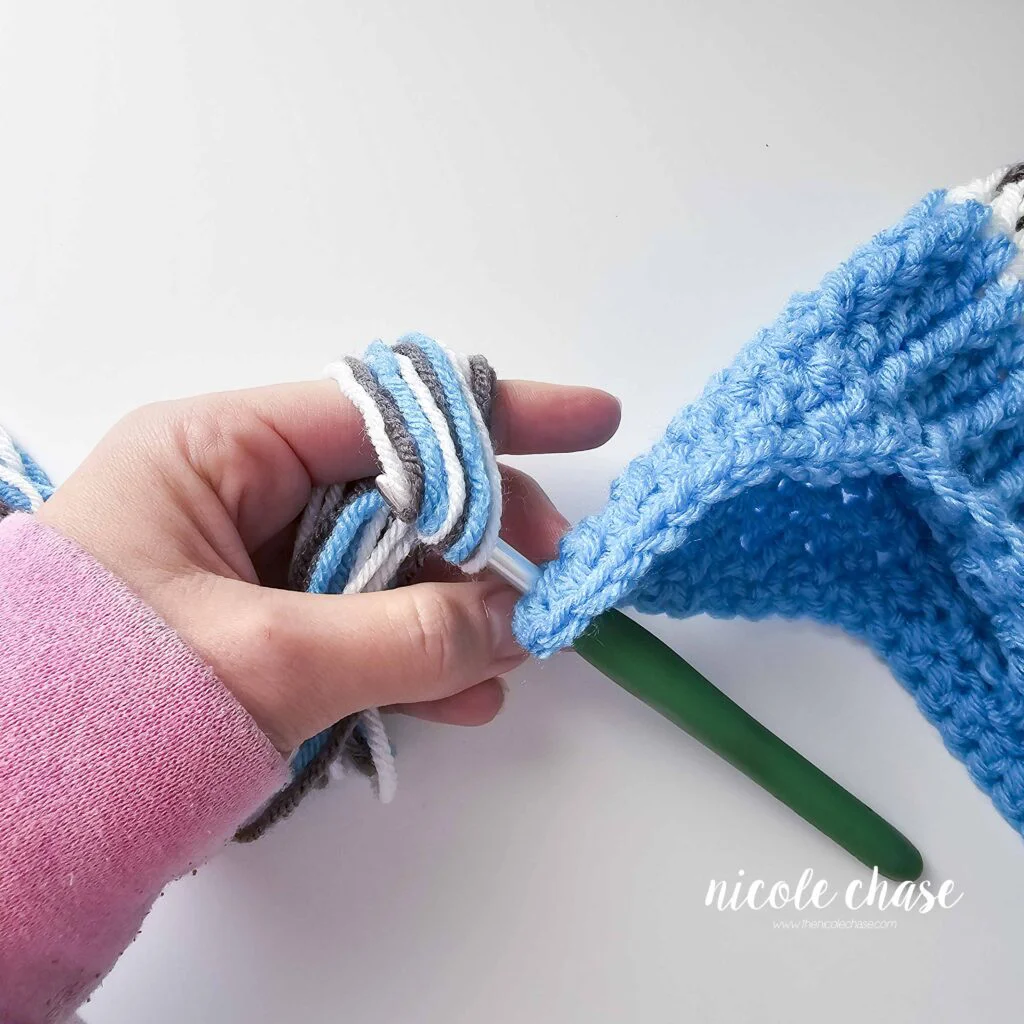 Adding the strands of yarn to make tassels on the crochet hat with earflaps